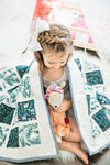 little-girl-with-braided-bow-hair-holding-doll-under-christmas-quilt